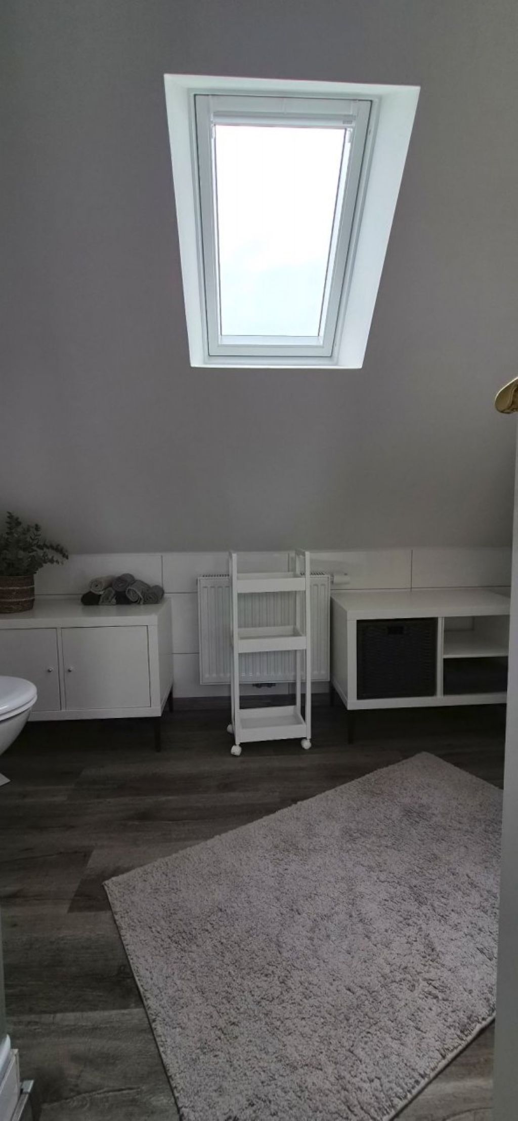 Quarto com claraboia, mobiliário branco, radiador e tapete cinza.