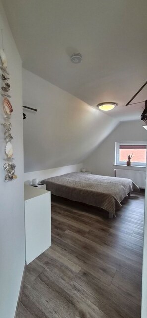 A bedroom with a sloped ceiling, a bed, a window with a view, and a wall-mounted shelf with decorative items. - Relax by the Water – Vacation Home with Its Own Boat Dock in Emden (Emden)