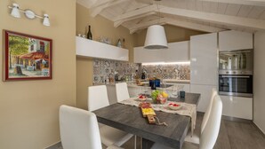 Uma cozinha moderna com armários brancos, uma mesa de jantar posta com pratos e copos, e um lustre pendurado acima.