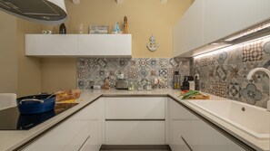 Eine Küche mit weißen Schränken, einer gemusterten Spritzschutzwand und verschiedenen Geräten und Gegenständen auf der Arbeitsfläche.