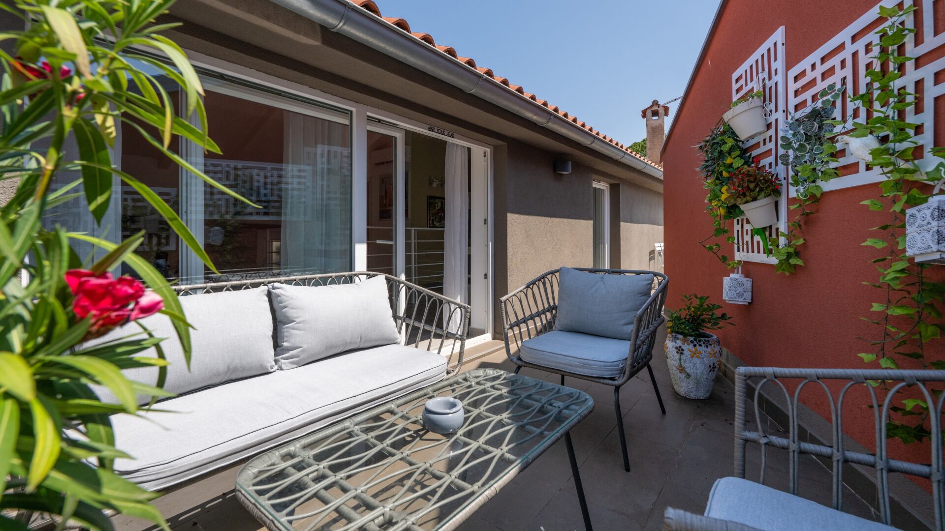An outdoor seating area with a sofa and chairs, a table, and potted plants.