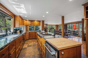 A spacious kitchen with wooden cabinets, a central island, and a large window overlooking a deck. - S7610 | 10 Deschutes (Sunriver)