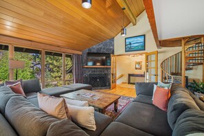 A spacious living room with a large sectional sofa, a fireplace, and a view of the outdoors through large windows. - S7610 | 10 Deschutes (Sunriver)