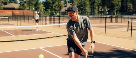 A tennis court with a net, a player in a cap and sunglasses, and another player in the background.