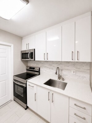 A modern kitchen with white cabinets, stainless steel appliances, and a marble backsplash.