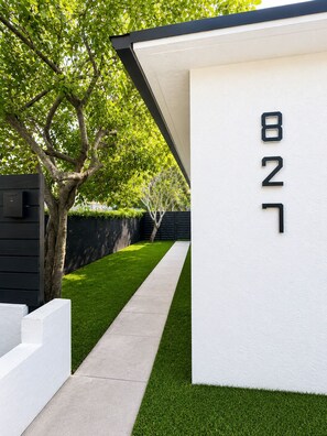 A modern building with a white exterior wall and a black roof. A tree with green leaves is visible in the background.