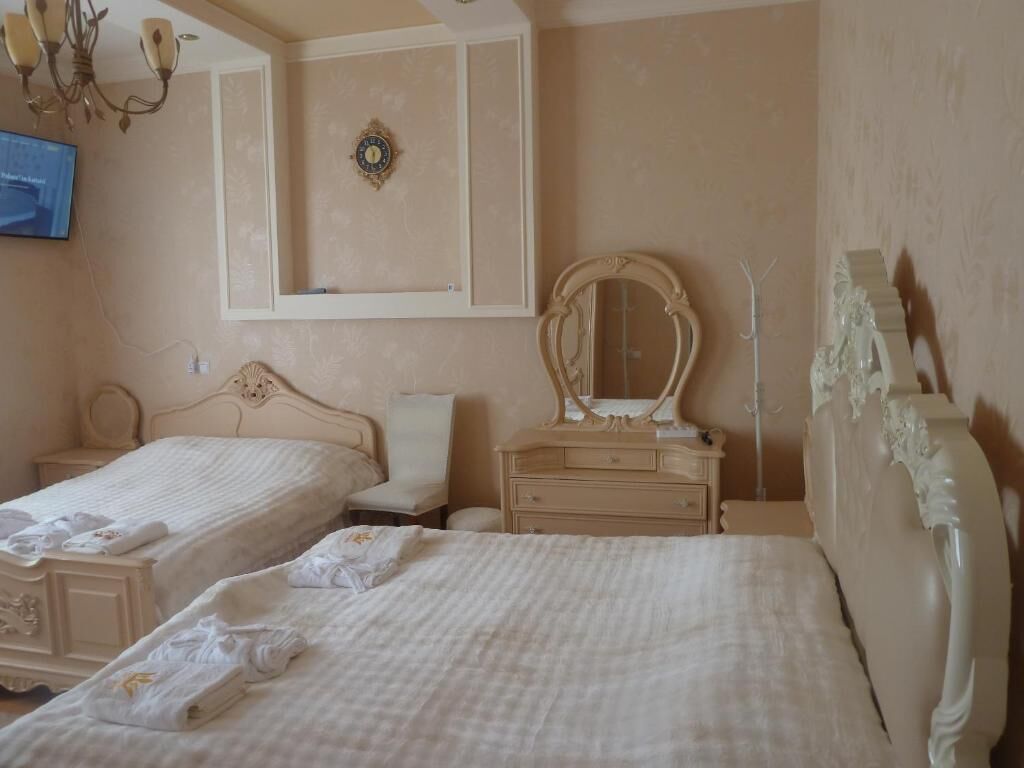Habitación de hotel con dos camas, un tocador con espejo, un reloj de pared y una televisión.