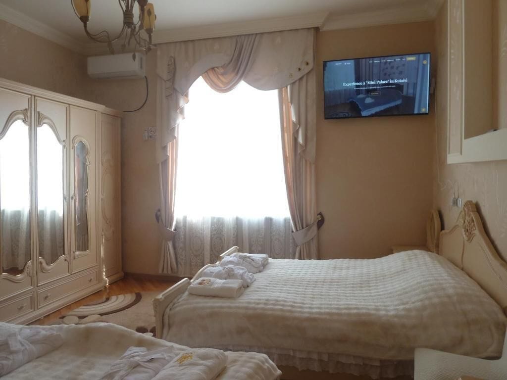 Habitación de hotel con dos camas, un televisor montado en la pared y un gran ventanal con cortinas.