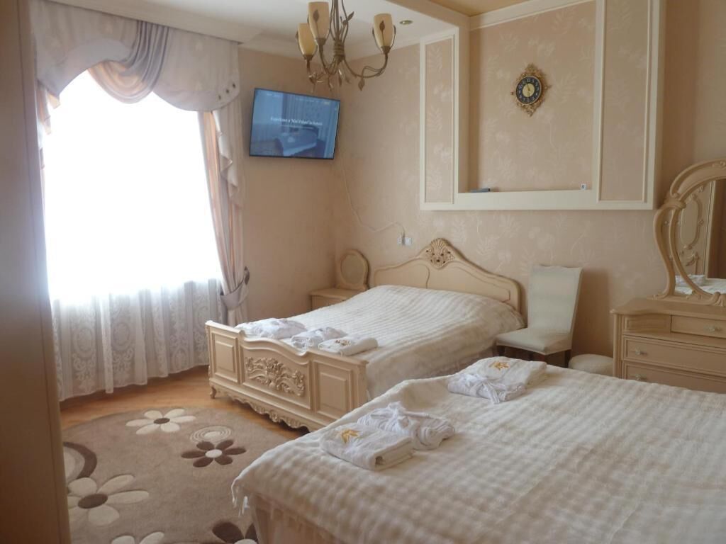 A hotel room with two beds, a television, a chandelier, and a mirror.