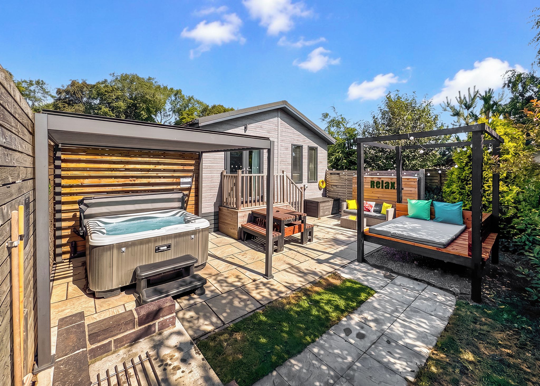 A backyard with a hot tub, a wooden deck, a pergola with seating, and a small house.