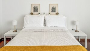 A neatly made bed with white linens, two bedside tables with lamps, and two framed pictures on the wall.