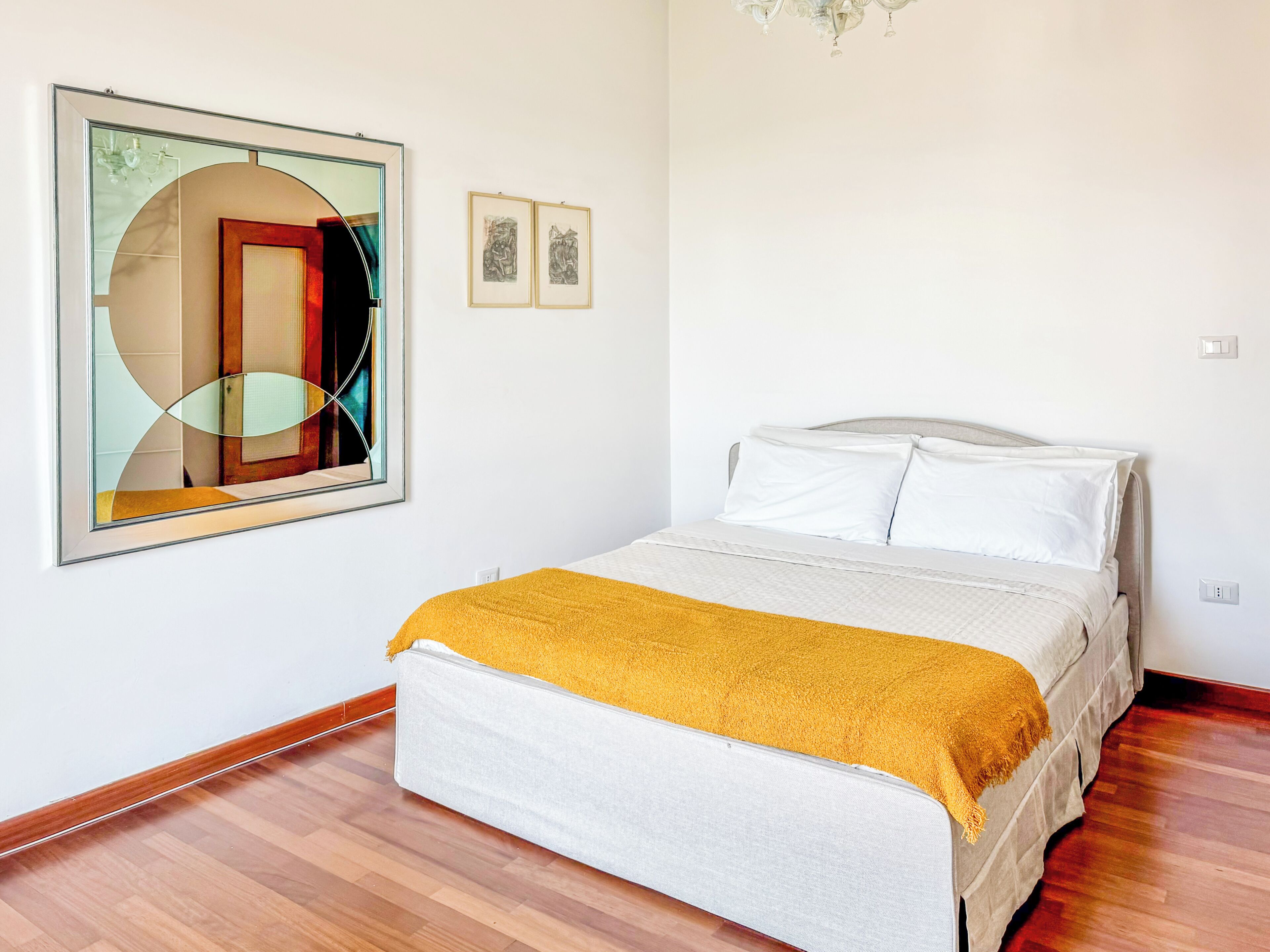 A bedroom with a bed, a large abstract painting, and two smaller framed pictures on the wall.