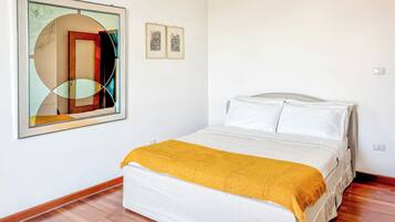 A bedroom with a bed, a large abstract painting, and two smaller framed pictures on the wall.