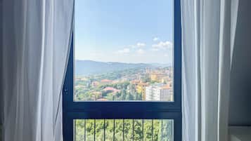 A window with a view of a cityscape, curtains partially drawn, and a balcony railing.