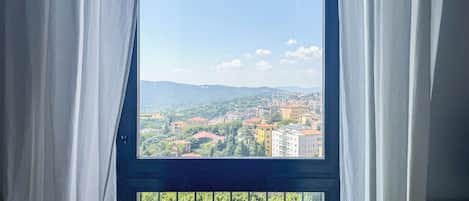 A window with a view of a cityscape, curtains partially drawn, and a balcony railing.