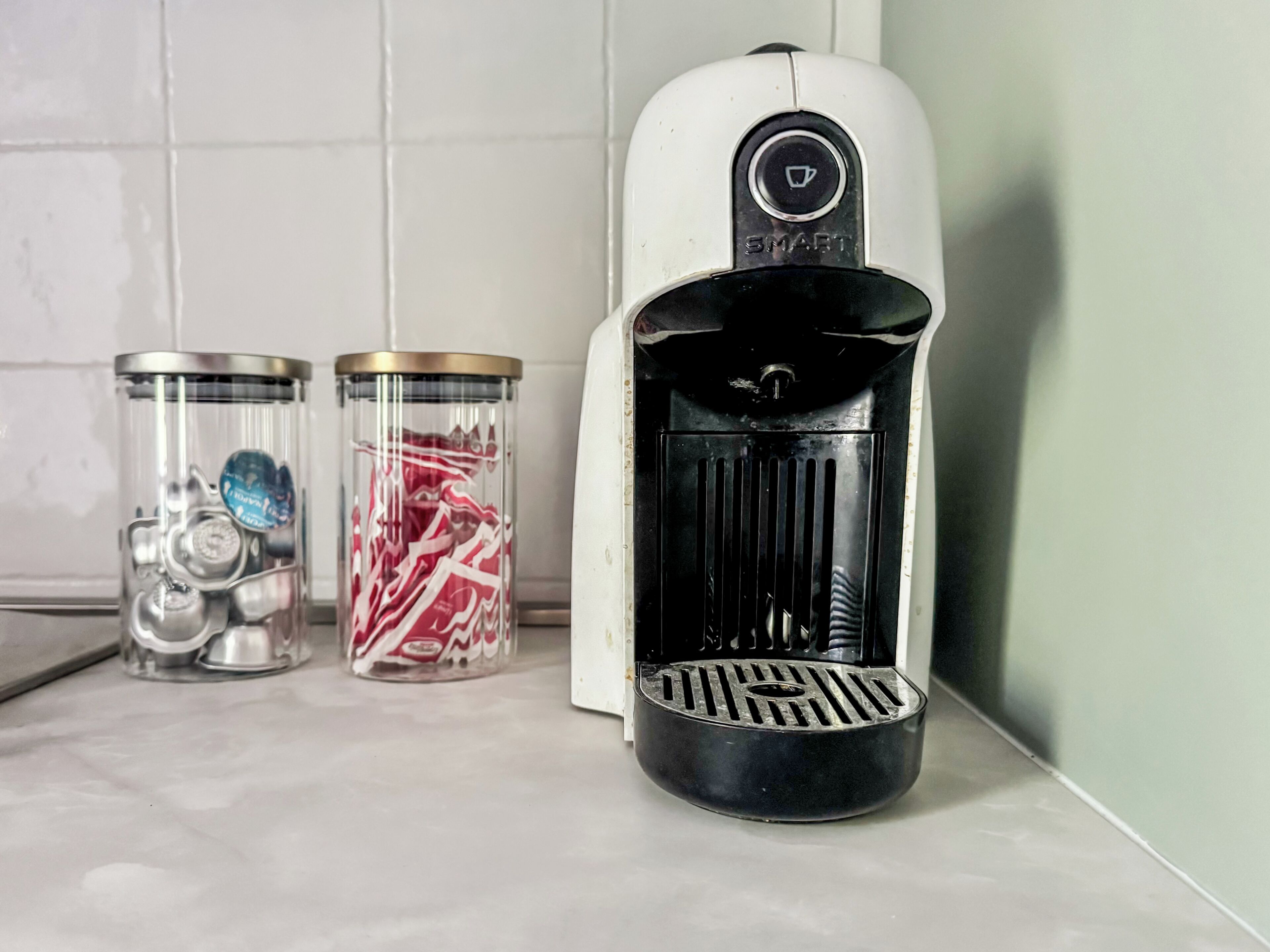 Een koffiezetapparaat met een 'SMART' aanduiding, twee glazen potten met deksels, en een witte betegelde muur.