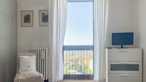 A bedroom with a bed, a radiator, a TV, and a window with curtains.