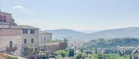 A traditional stone building with a tiled roof, surrounded by greenery and a distant view of a town.