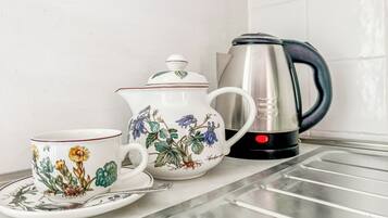 Una encimera de cocina con una tetera blanca, una taza a juego y un hervidor de acero inoxidable.