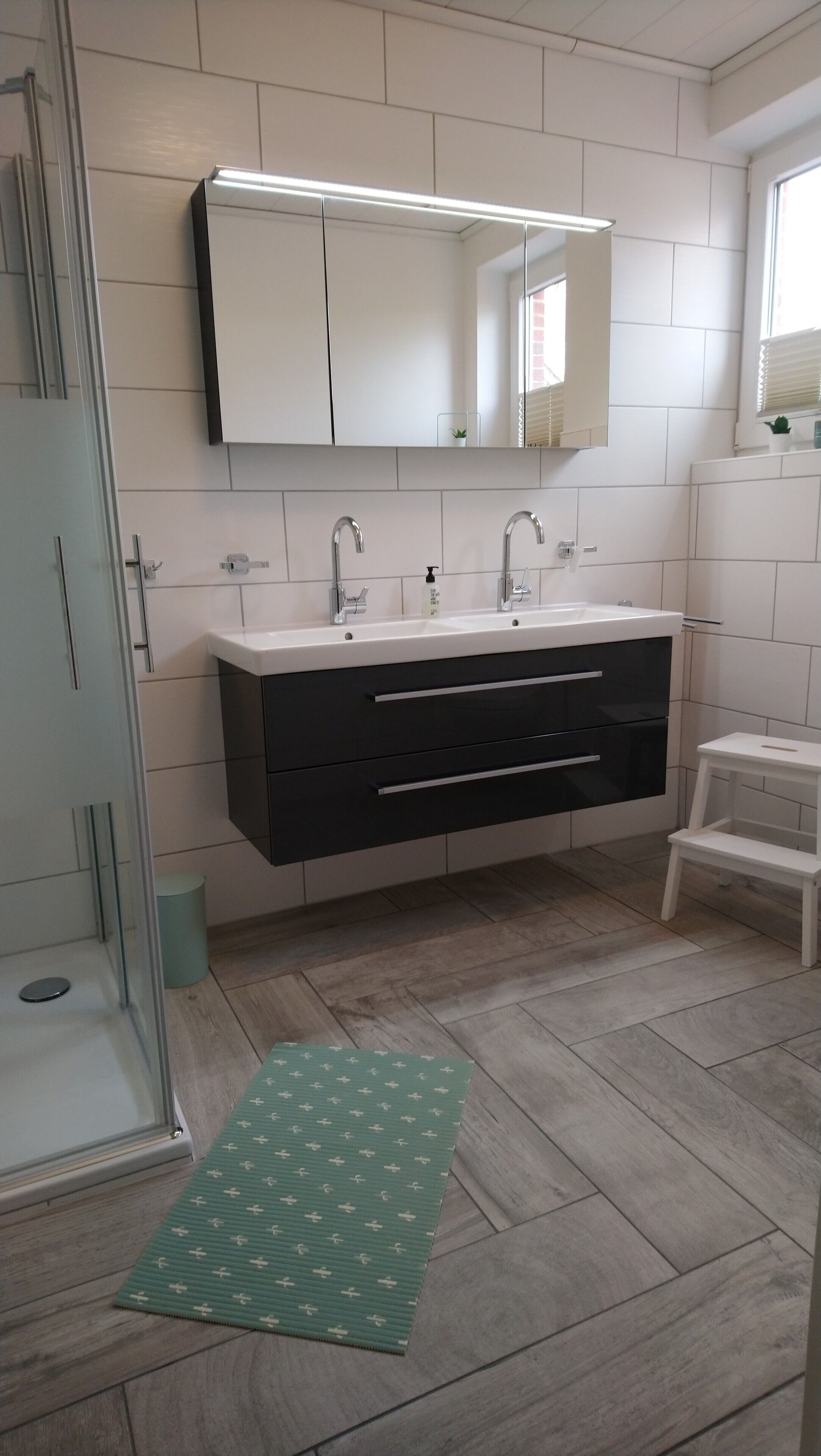 Ein Badezimmer mit modernem Design, ausgestattet mit einem großen Spiegel, einem Doppelwaschbecken und einer begehbaren Dusche.