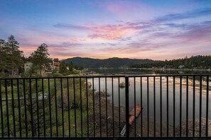A lakeside view with a wooden dock, a metal railing, and a forested hillside in the background. - Lakefront Chalet in Boulder Bay! | Hot Tub | Fire Pit | Amazing Lake Views (Big Bear Lake)