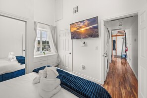 A hotel room with a bed, a window with curtains, a painting on the wall, and a hallway leading to another room. - Lakefront Chalet in Boulder Bay! | Hot Tub | Fire Pit | Amazing Lake Views (Big Bear Lake)