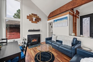 A modern living room with a fireplace, a blue leather sofa, and a wooden ceiling beam. - Lakefront Chalet in Boulder Bay! | Hot Tub | Fire Pit | Amazing Lake Views (Big Bear Lake)