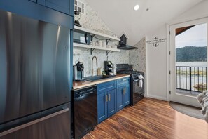 A modern kitchen with a stainless steel refrigerator, blue cabinets, a wooden countertop, and a view of a lake through a glass door. - Lakefront Boulder Bay Chalet with Hot Tub, A/C, Fire Pit & Panoramic Views (Big Bear Lake)