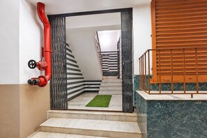 A staircase with a red pipe on the left, a green carpet, and a wooden door on the right. - Deluxe Ayush Villa (Kolkata)