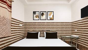 A hotel room with a bed, a small table, and three framed artworks on the wall.
