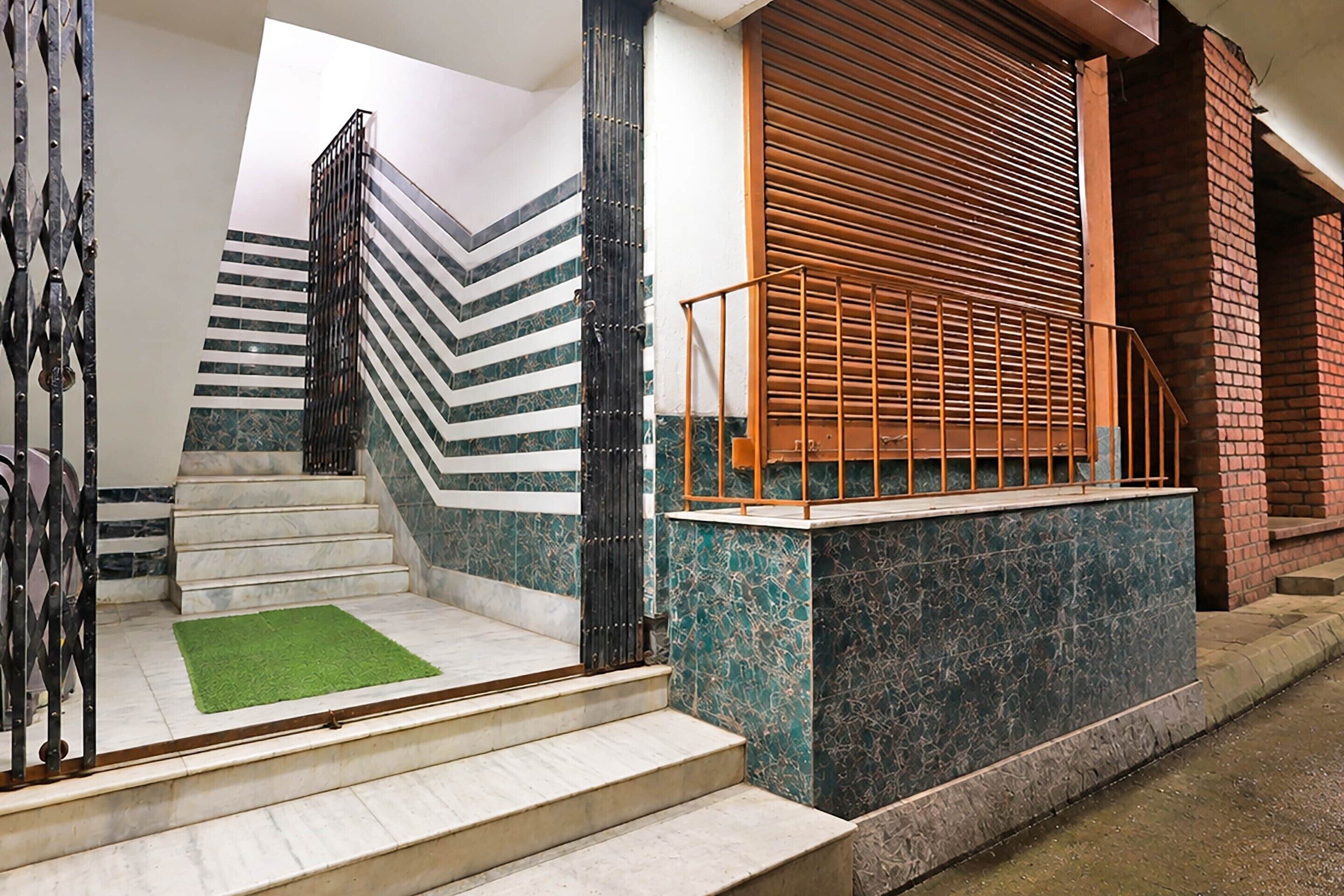 A staircase with a metal railing, a green carpet, and a brick wall.