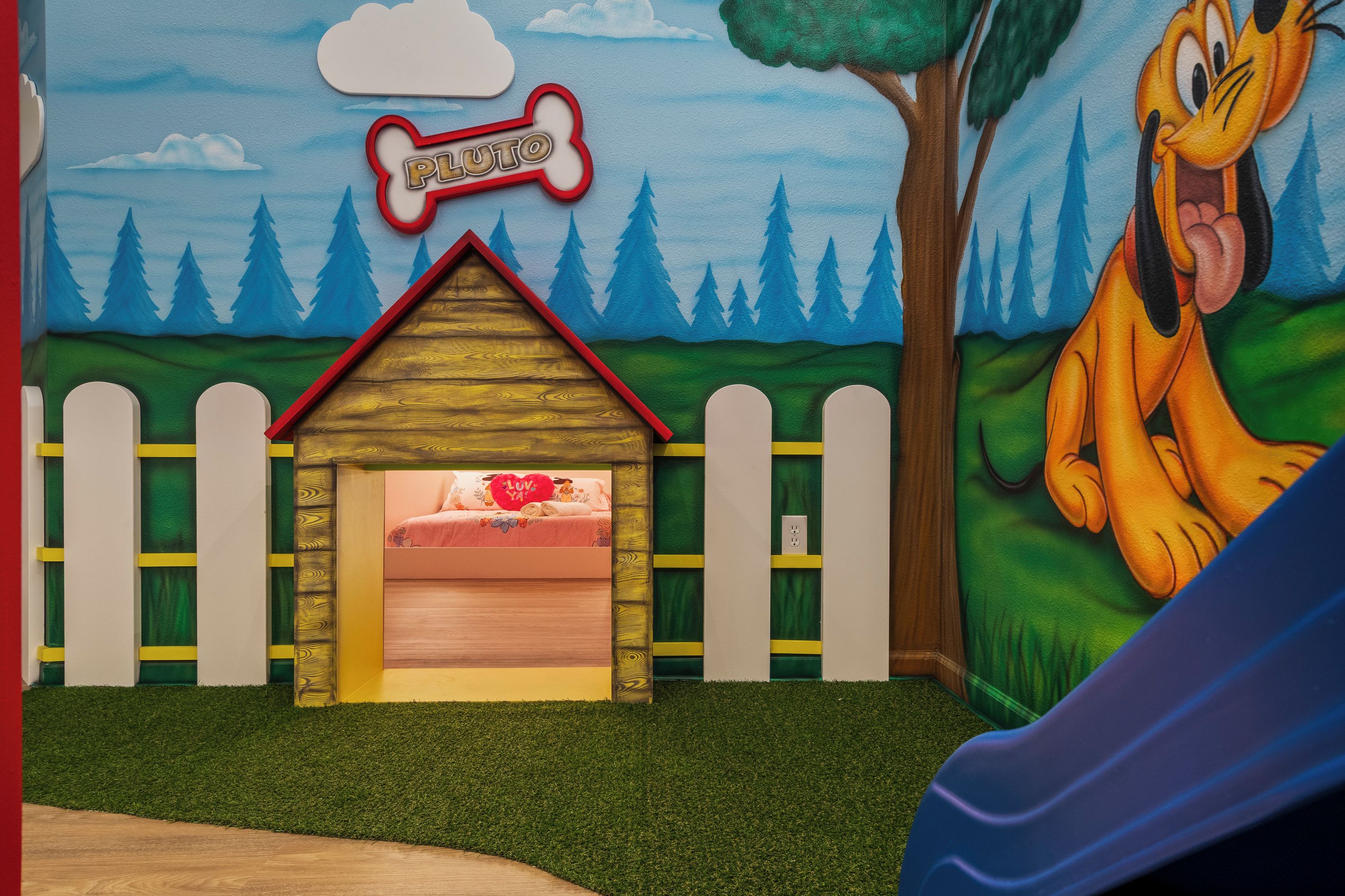Una sala de juegos infantiles con una cama, una casita de madera y un personaje de caricatura.