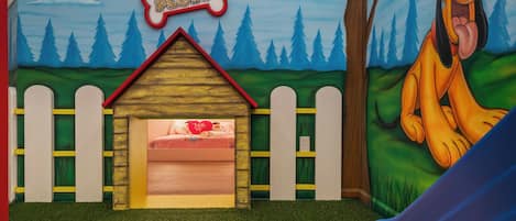Una sala de juegos infantiles con una cama, una casita de madera y un personaje de caricatura.