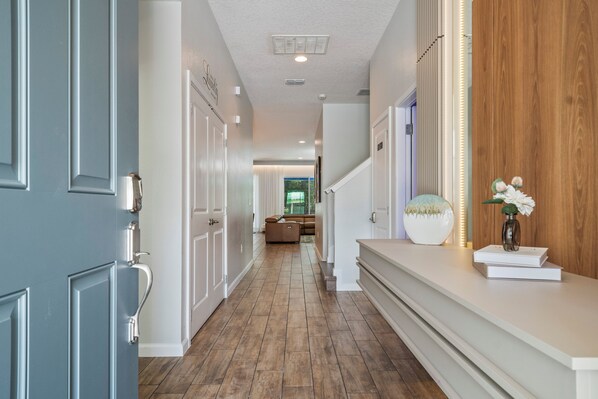 Un couloir doté d’un plancher en bois, de murs blancs et d’un mur d’accent en bois. Il y a une porte sur la gauche et un comptoir avec un vase de fleurs sur la droite.