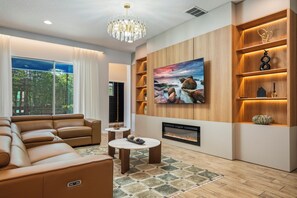 Un salon moderne avec un canapé en cuir, une cheminée, un téléviseur fixé au mur et des étagères en bois ornées d’objets décoratifs.