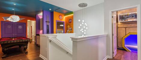 Une pièce avec une table de billard, un escalier et une porte donnant sur une salle de jeux.