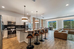 Une cuisine moderne dotée d’appareils électroménagers en acier inoxydable, d’un îlot central avec des tabourets de bar et d’un coin repas offrant une vue sur l’extérieur.