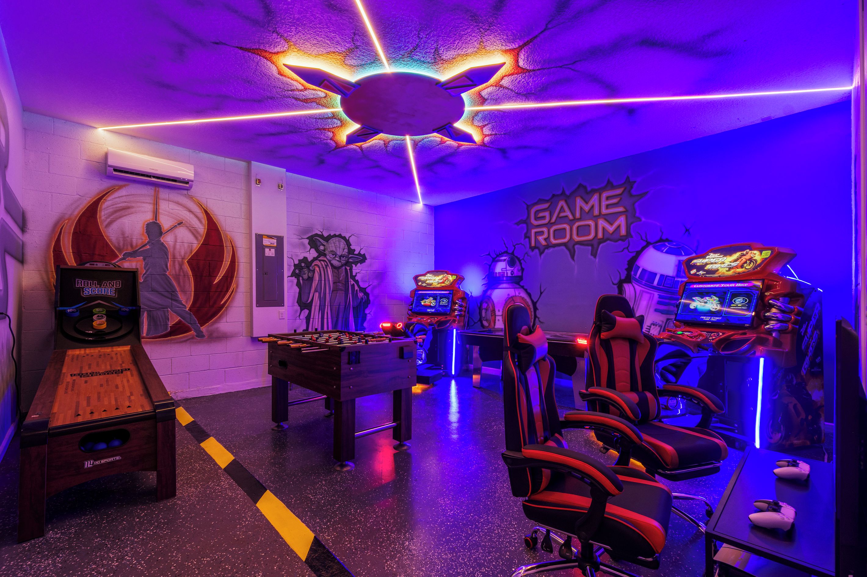 A gaming room with multiple foosball tables, racing simulators, and gaming chairs.