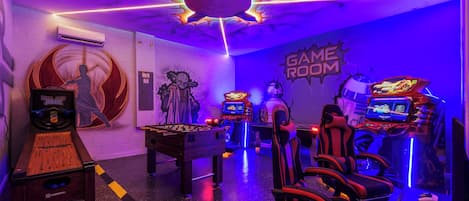 A gaming room with multiple foosball tables, racing simulators, and gaming chairs.