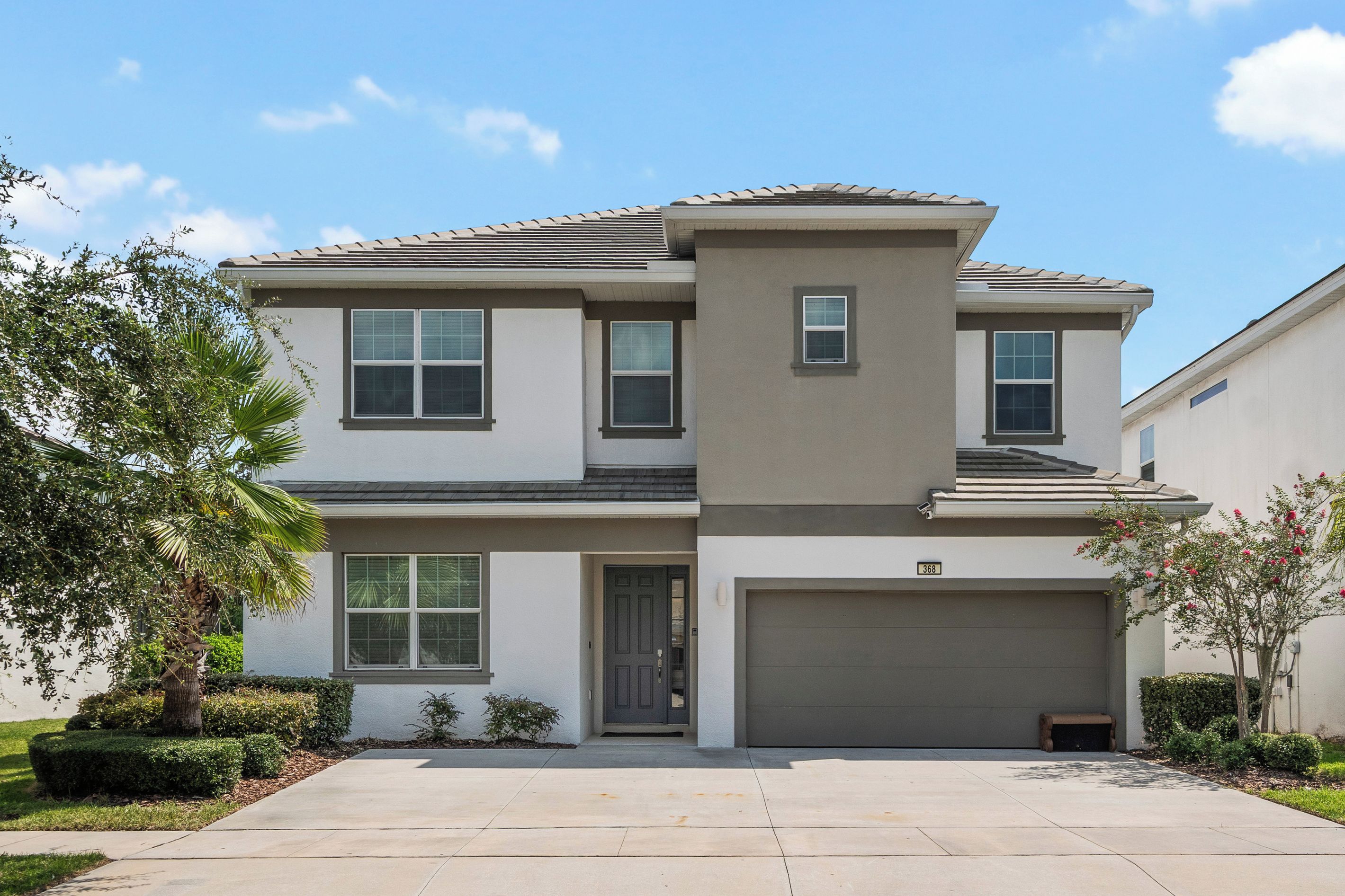 A two-story residential building with a garage, a small porch, and a well-maintained lawn.