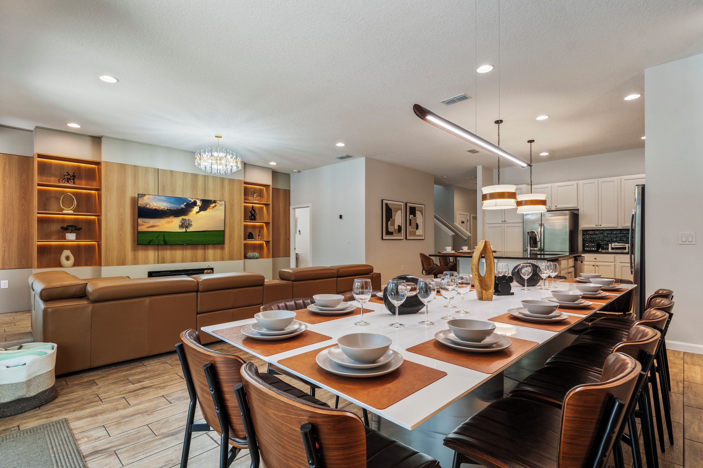A modern kitchen with stainless steel appliances, a dining area with a long table set for six, and a cozy seating area with a large flat-screen TV.