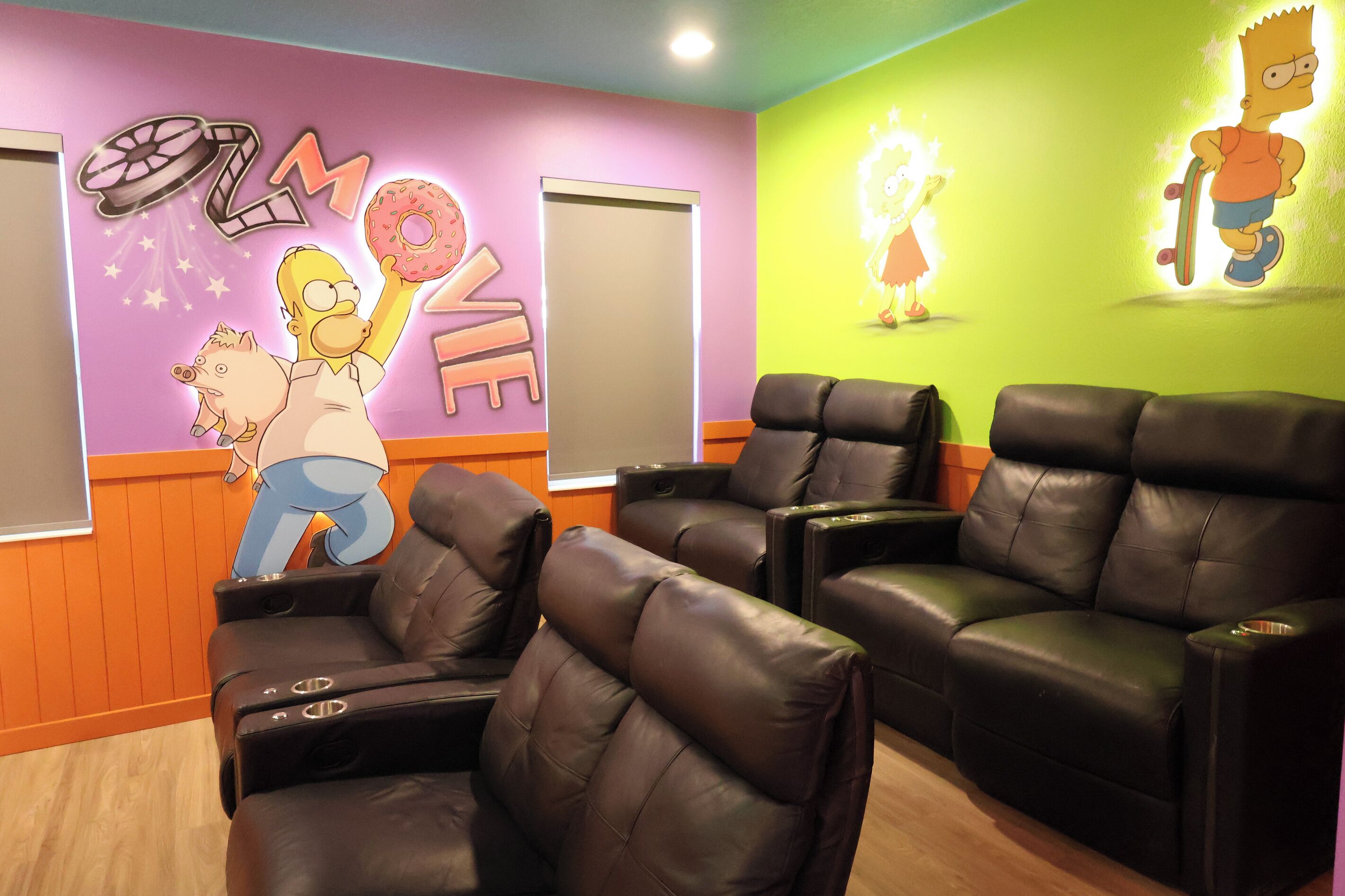 A room with black leather chairs, a wall with cartoon characters, and a wooden floor.