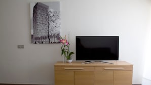 A modern living room with a flat-screen TV on a wooden cabinet, a vase with flowers, and a cityscape painting on the wall. - Vacation Studio 'Terraza A La Playa' with Wi-Fi (Las Palmas de Gran Canaria)