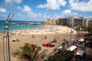 Una playa con mucha gente, un muelle y edificios al fondo.
