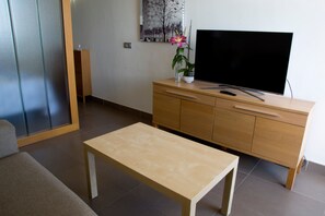 Ein Wohnzimmer mit einem TV-Schrank aus Holz, einem Flachbildfernseher, einem kleinen Tisch und einer Couch.