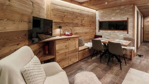 A cozy room with a wooden interior, a sofa, a dining table with chairs, and a television mounted on the wall. - Apartment at the foot of the legendary Matterhorn in the Cervina–Zermatt area. (Breuil-Cervinia)