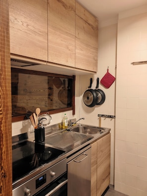 Eine moderne Küche mit Holzschränken, Edelstahlgeräten und einer abgehängten Topfablage.