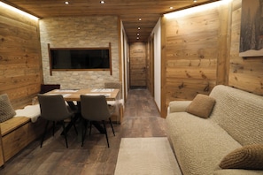 Un intérieur chaleureux avec une table à manger en bois, des chaises, un canapé et un mur en pierre.