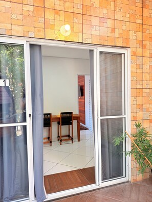 Um quarto com porta de vidro deslizante, uma mesa de madeira com cadeiras e piso ladrilhado.