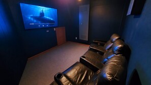 A home theater room with a large flat-screen TV, leather reclining chairs, and a carpeted floor. - Spectacular Sunrises, Pool, Hot Tub, Theater Room, Office, SN9317 (Nags Head)